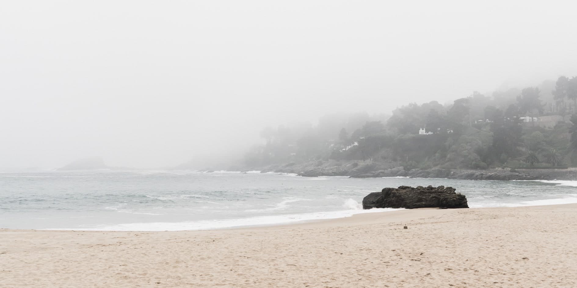 Playa con niebla, roca en la orilla a la derecha, cerro con casas y árboles entre la bruma. Agua #P3, fotografía de Cristian Letelier, edición limitada