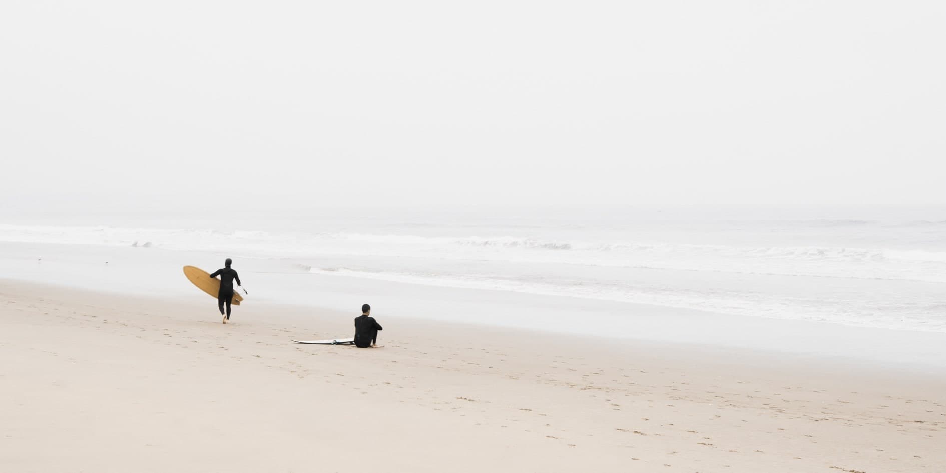 Dos surfistas en la arena: uno de pie con tabla amarilla, otro sentado; mar blanquecino. Agua #P5, fotografía de Cristian Letelier, edición limitada