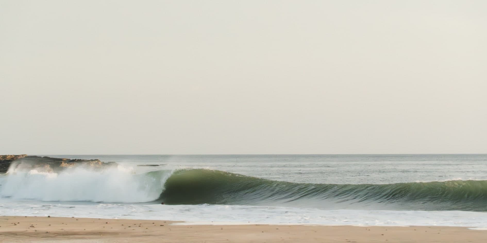 Ola verde rompiendo en tubo, cielo pálido, arena en primer plano. Agua #P11, fotografía de Cristian Letelier, edición limitada