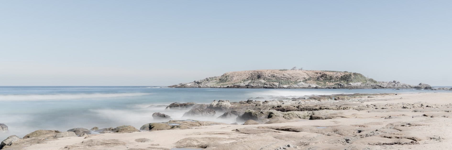 Panorámica: isla rocosa al fondo, roquerío en primer plano, mar sedoso de larga exposición. Agua #P13, fotografía de Cristian Letelier, edición limitada
