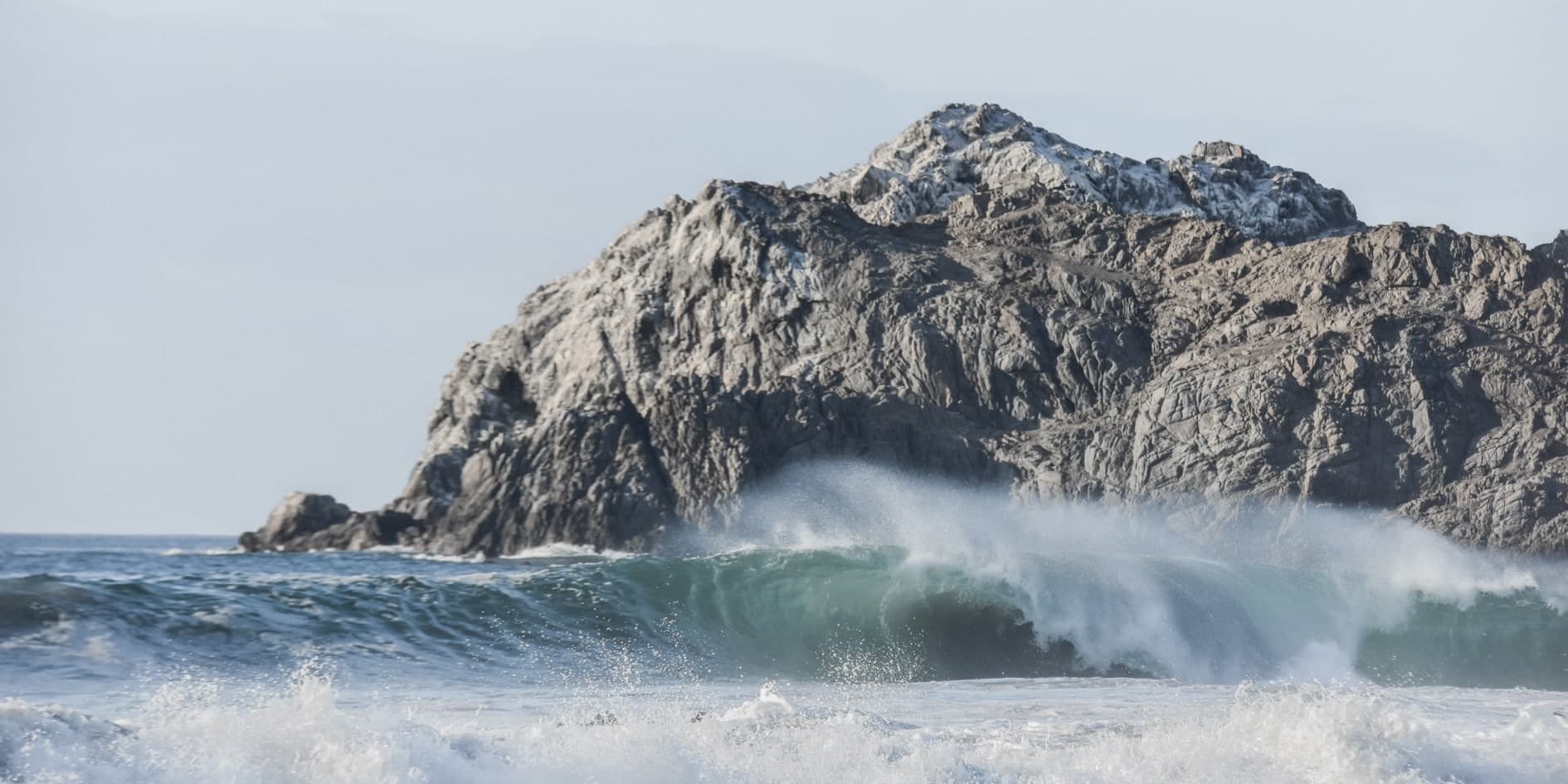Ola grande rompiendo con spray frente a un cerro rocoso escarpado. Agua #P17, fotografía de Cristian Letelier, edición limitada