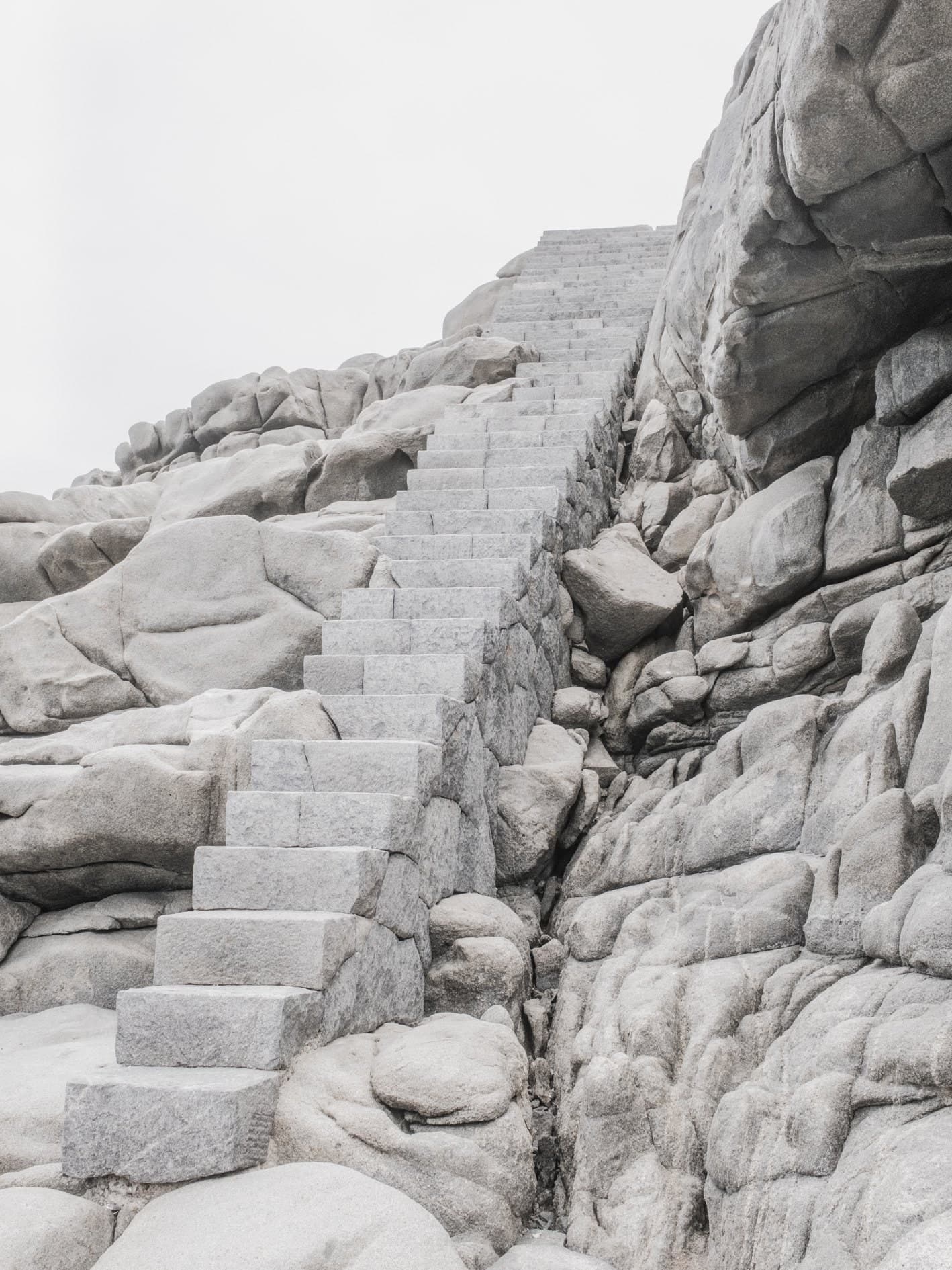 Vertical: escalera de piedra entre rocas graníticas claras, cielo blanco. Agua #P22, fotografía de Cristian Letelier, edición limitada