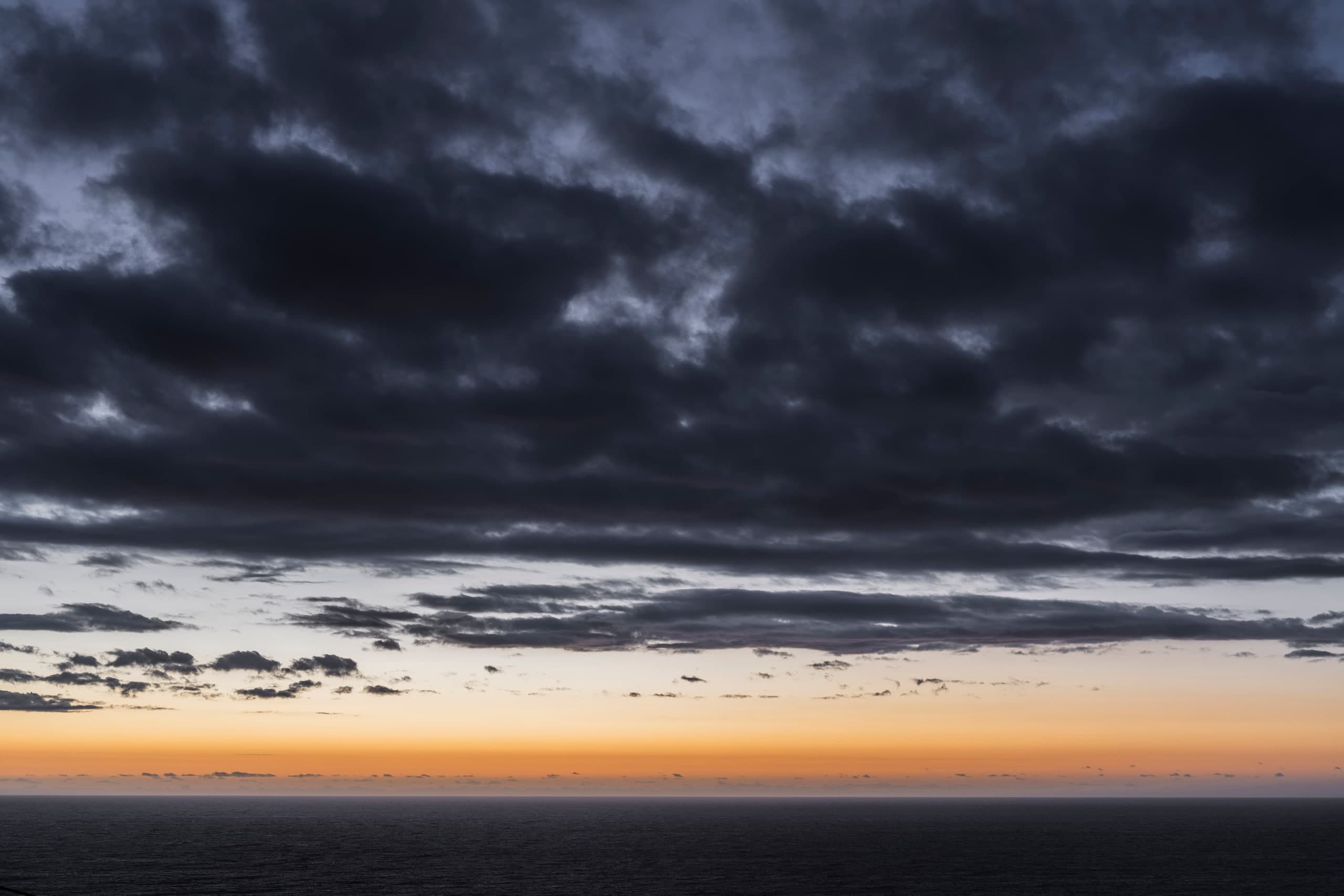 Nubes oscuras sobre el mar con una franja de luz cálida en el horizonte. Agua #P50, fotografía de Cristian Letelier, edición limitada
