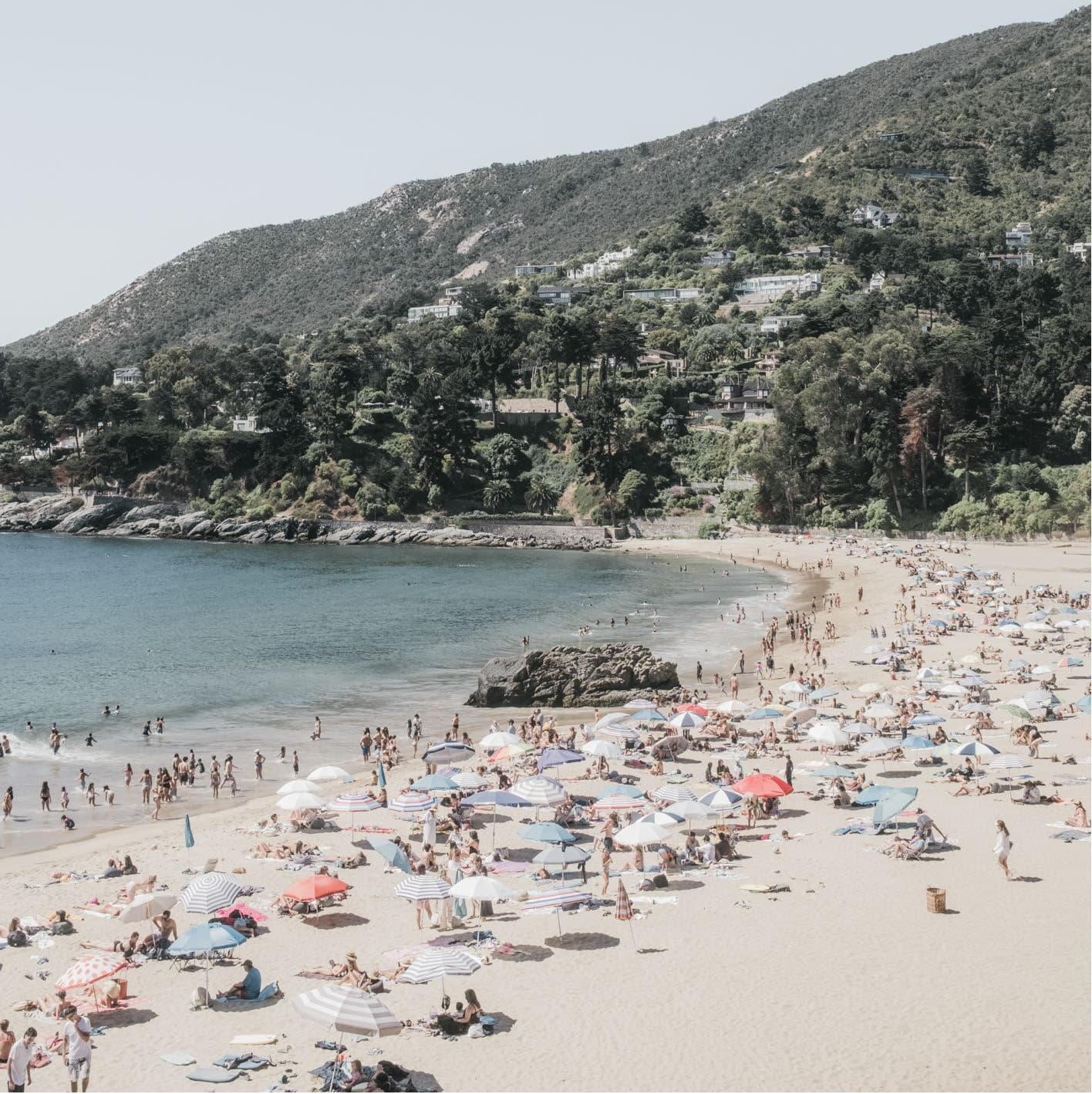 Cuadrada: playa muy concurrida con quitasoles de colores, cerro verde con casas, roca en el mar. Agua #P25, fotografía de Cristian Letelier, edición limitada