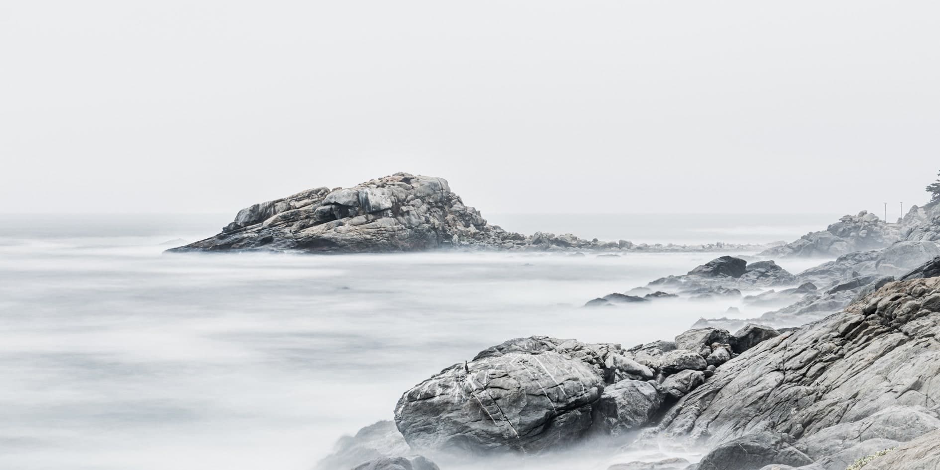 Roquerío con mar sedoso y niebla, isla rocosa al fondo, tonos desaturados casi B/N. Agua #P31, fotografía de Cristian Letelier, edición limitada