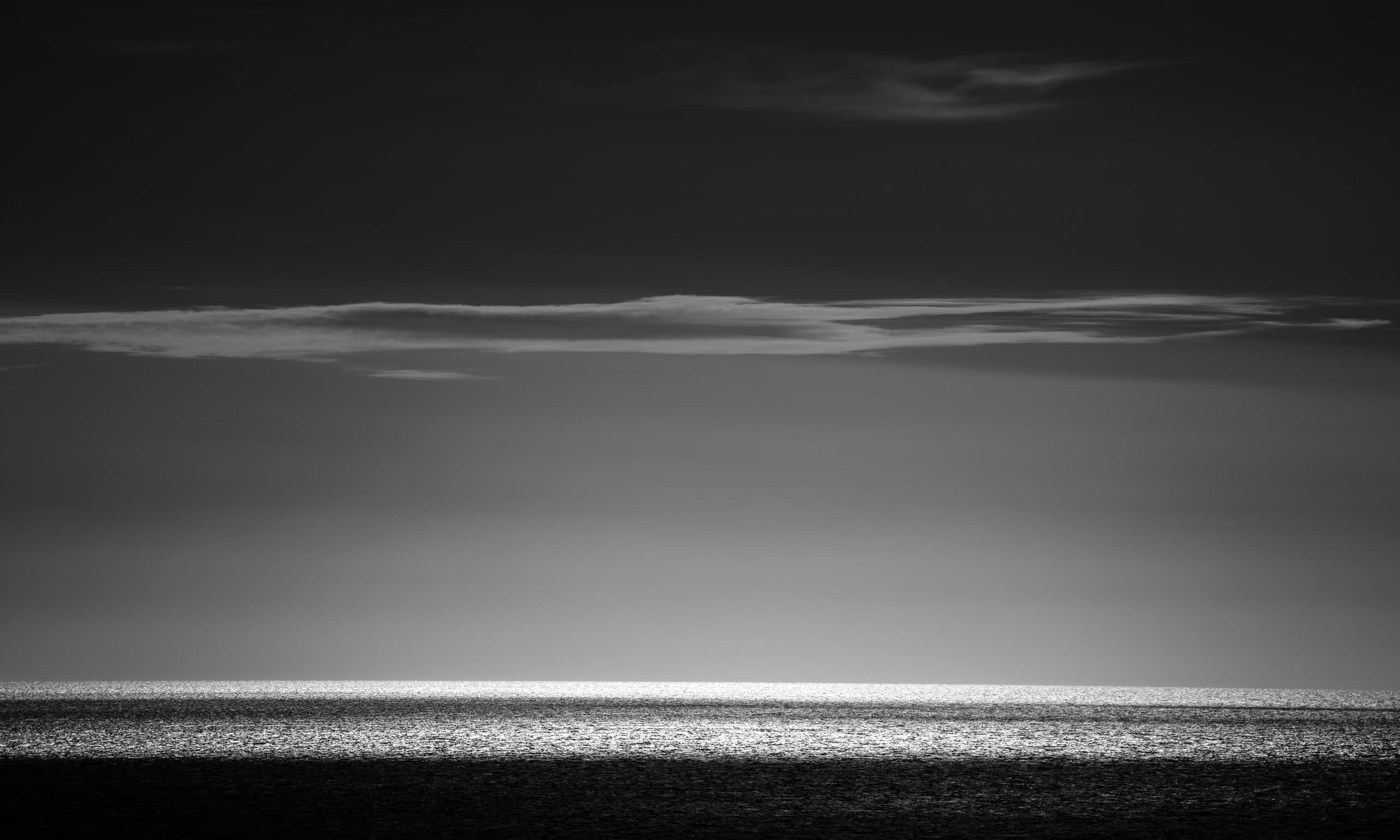 Mar en blanco y negro: franja de luz sobre el agua bajo un cielo oscuro con una nube fina. Agua #P47, fotografía de Cristian Letelier, edición limitada
