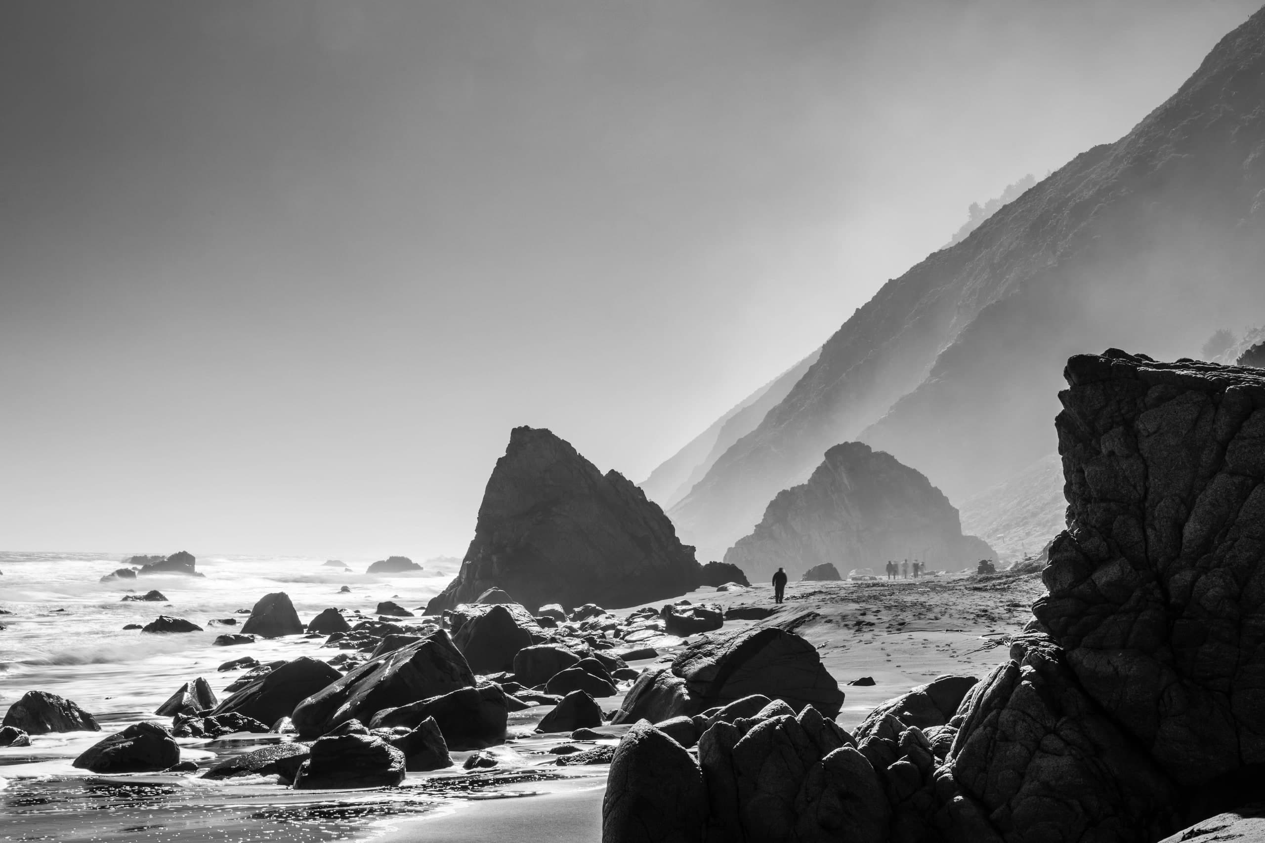 Costa en blanco y negro: rocas, oleaje y cerros en la bruma, una figura mínima en la orilla. Agua #P49, fotografía de Cristian Letelier, edición limitada