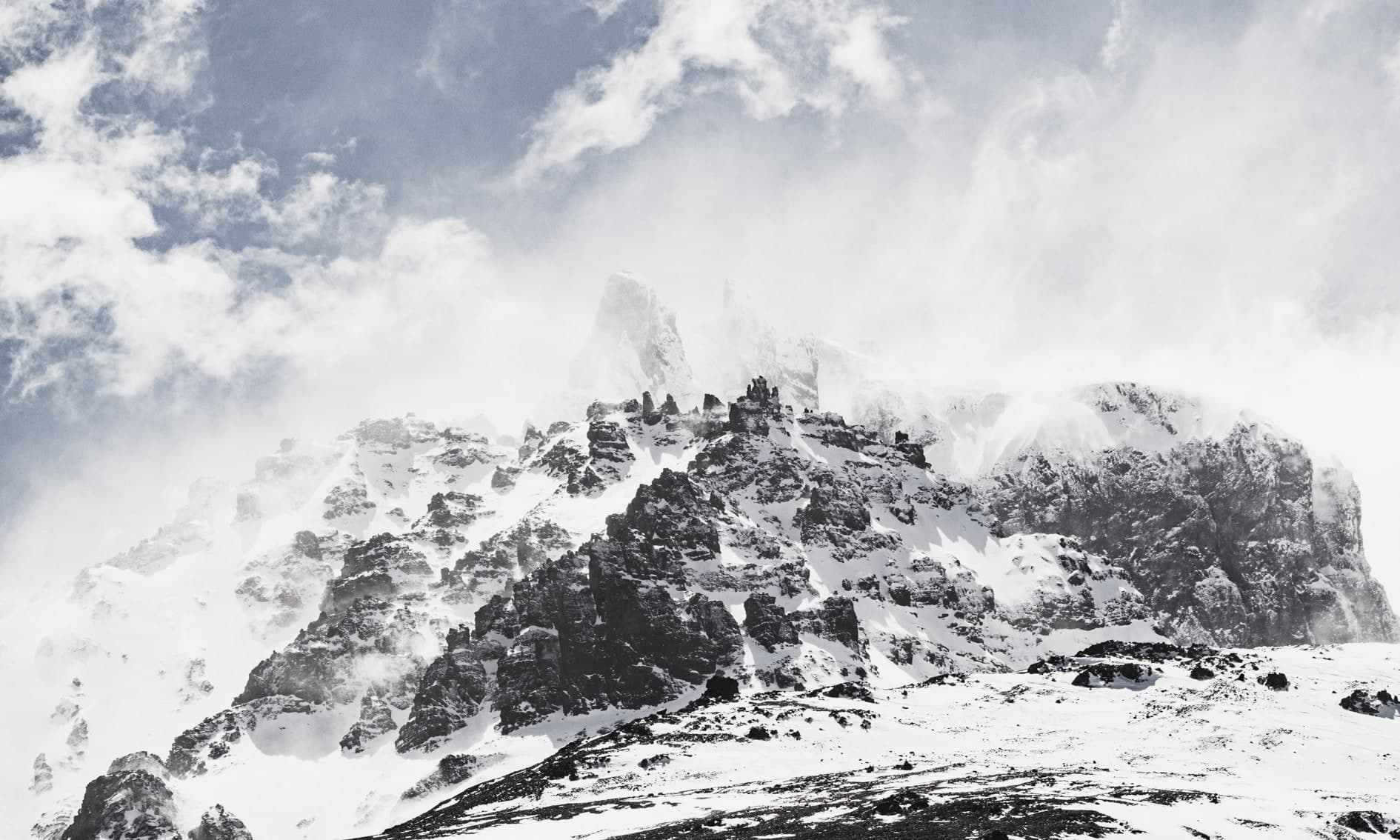 Cumbres rocosas oscuras nevadas con nubes dramáticas y cielo azul. Aire #C13, fotografía de Cristian Letelier, edición limitada