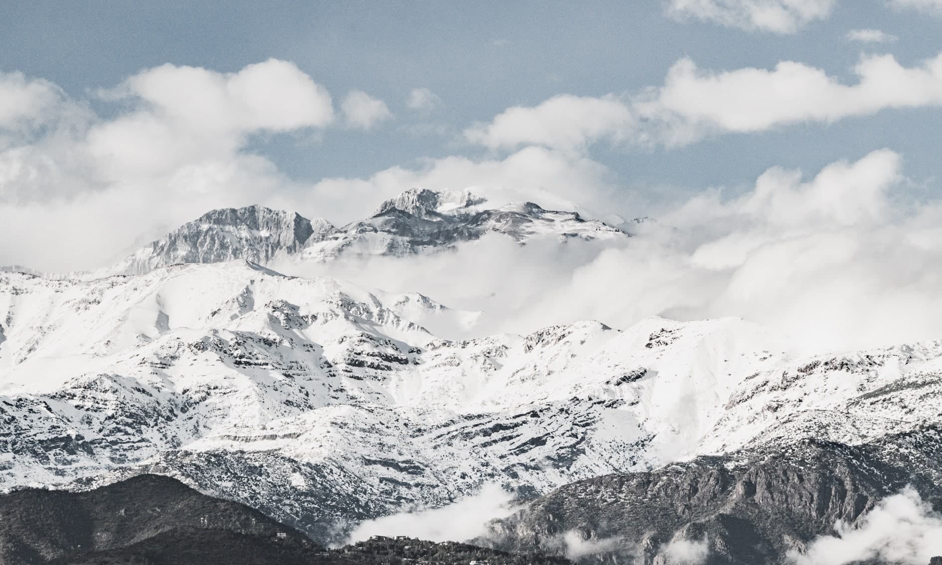 Cordillera nevada bajo cielo azul con nubes blancas, cerros oscuros al pie. Aire #C9, fotografía de Cristian Letelier, edición limitada