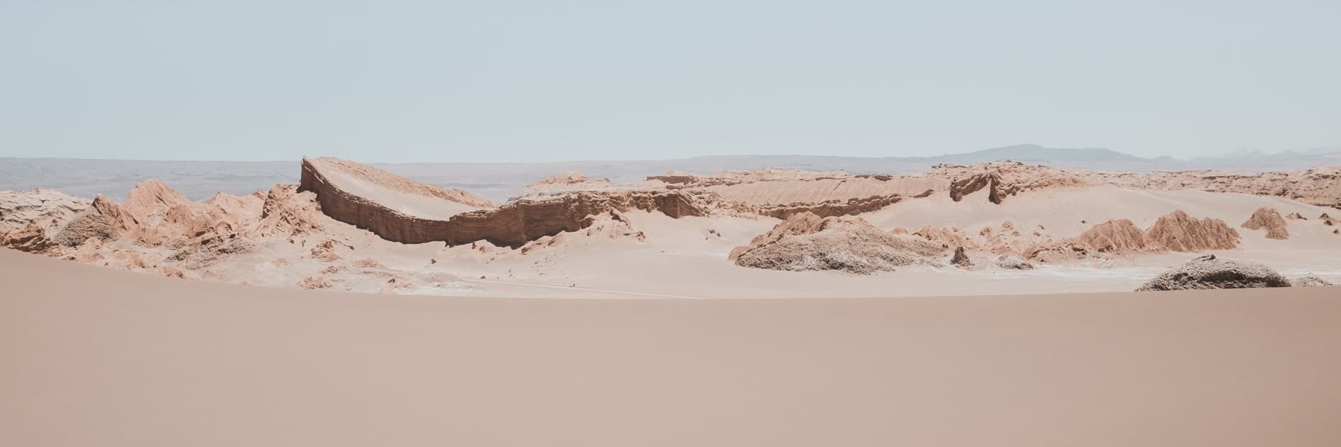 Panorámica de cordón rocoso rosado-beige tipo Valle de la Luna sobre arena lisa, cielo celeste pálido. Fuego #D4, fotografía de Cristian Letelier, edición limitada