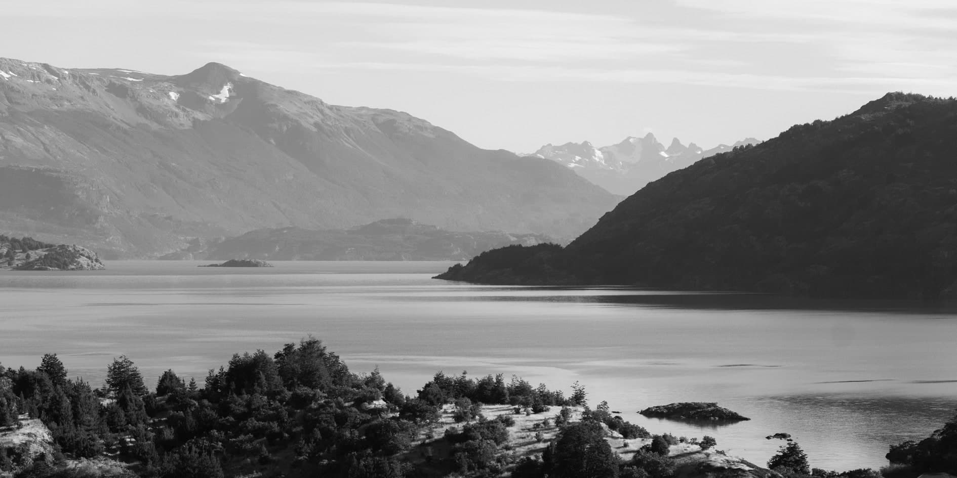 Lago entre montañas con bosque de coníferas en primer plano; blanco y negro. Tierra #S26, fotografía de Cristian Letelier, edición limitada