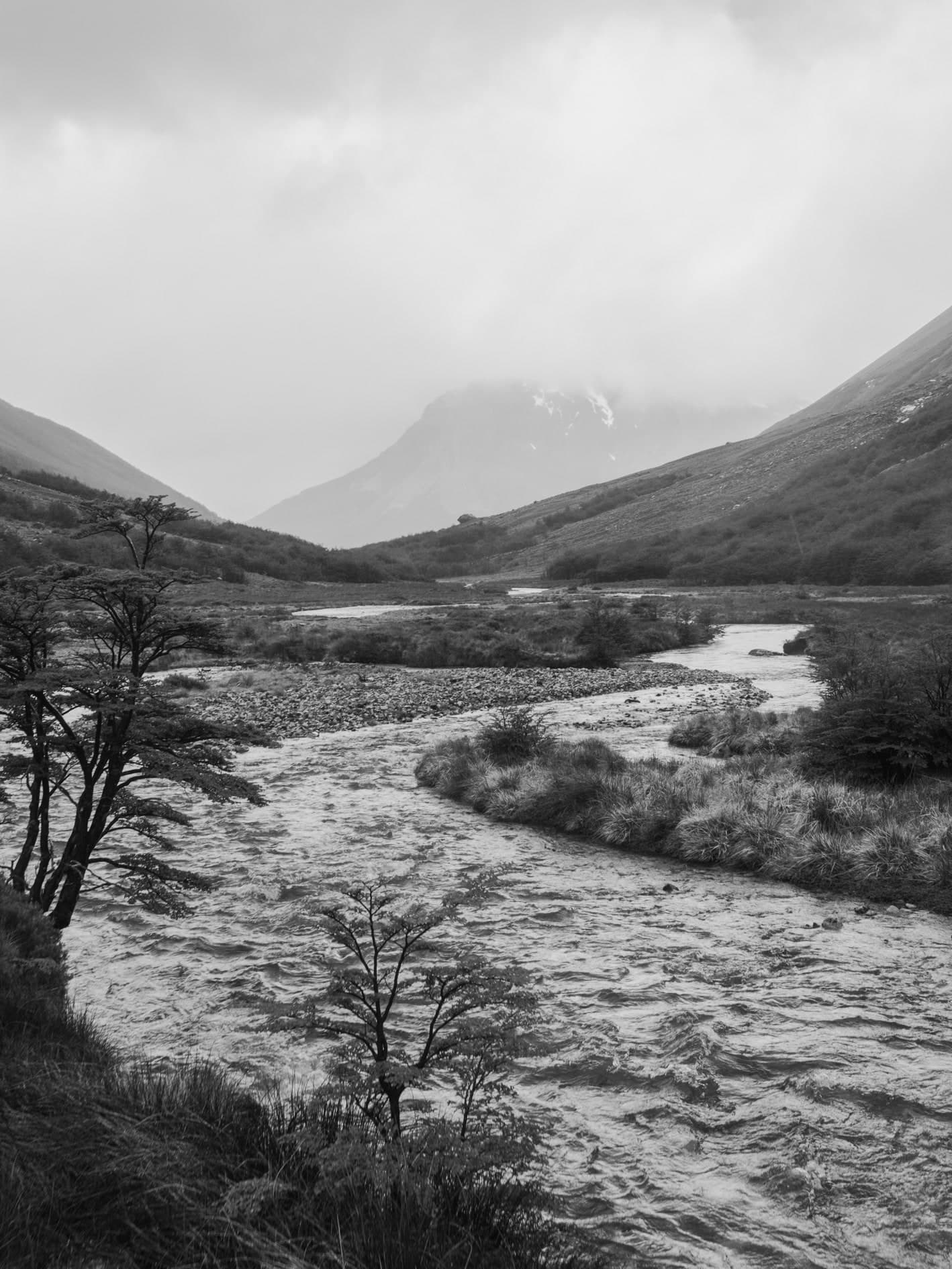 Río caudaloso en valle con montañas y niebla, árboles a la izquierda; formato vertical; blanco y negro. Tierra #S30, fotografía de Cristian Letelier, edición limitada