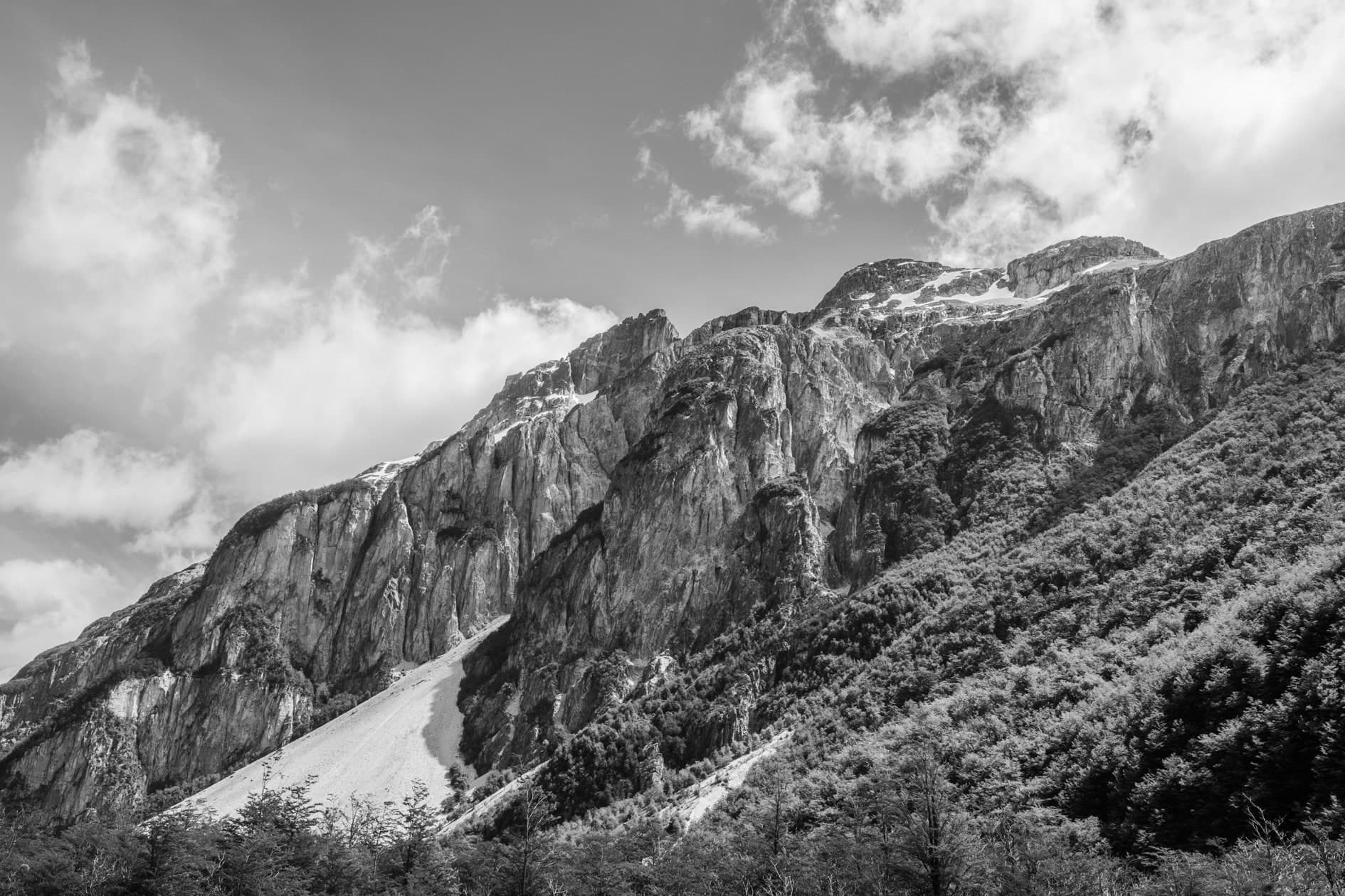 Pared de roca vertical con bosque en la ladera y nubes; blanco y negro. Tierra #S9, fotografía de Cristian Letelier, edición limitada